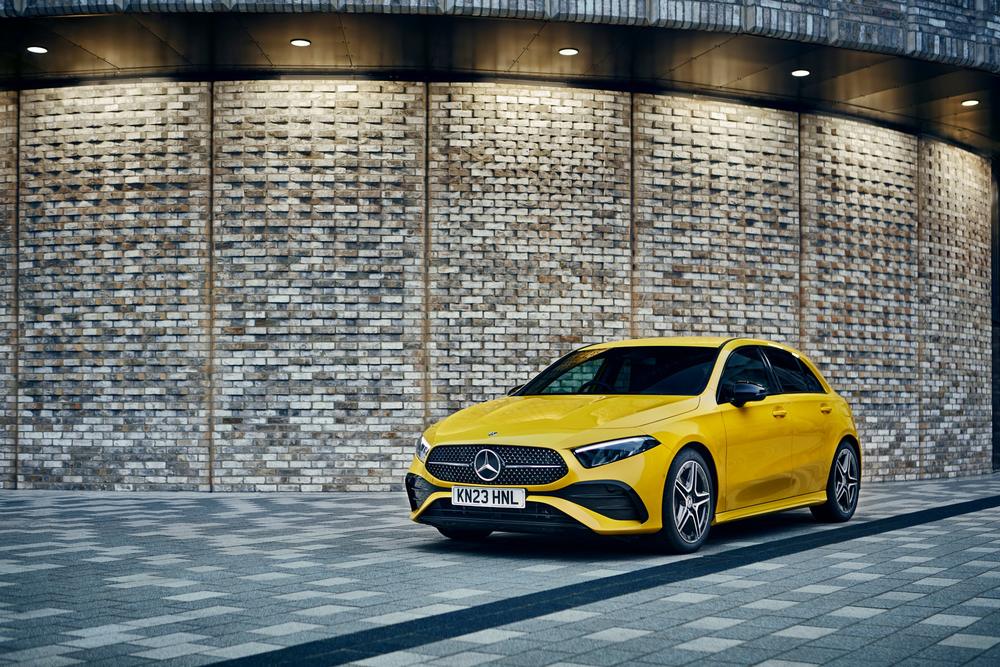 A yellow Mercedes-Benz A-Class hatchback parked on a paved street in front of a curved brick wall