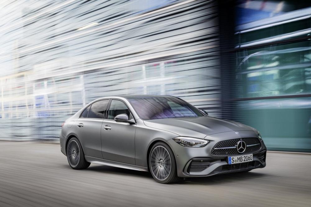 A matt grey Mercedes-Benz C-Class Sedan driving past a blurred glass building, seen from the front left