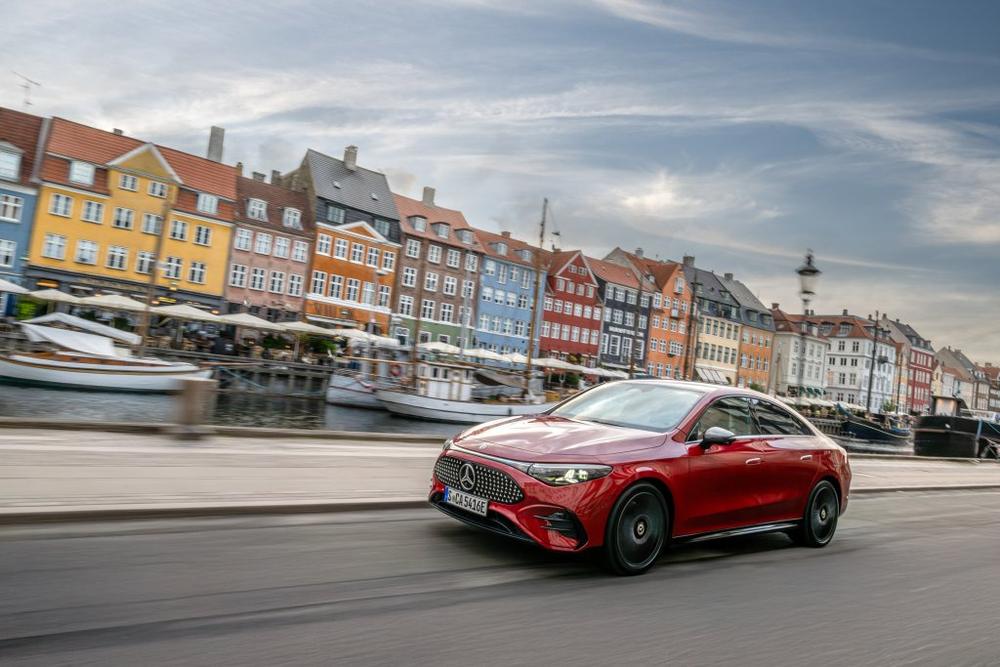 A red Mercedes-Benz CLA Sedan driving along a canal lined with colourful townhouses