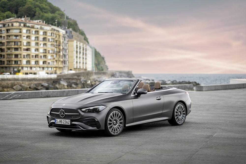 A graphite grey Mercedes-Benz CLE Cabriolet with its roof open, parked on a seafront promenade