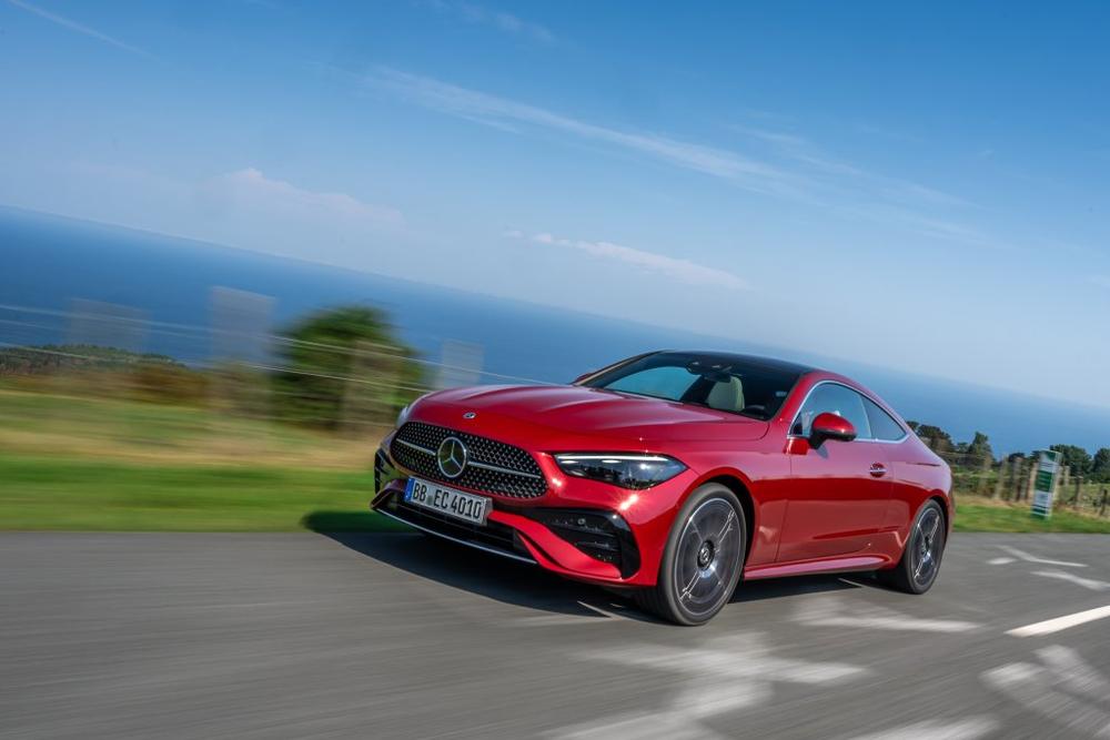 A red Mercedes-Benz CLE Coupé driving along a coastal road with the sea behind it