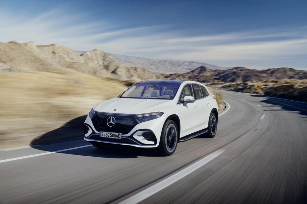 A white Mercedes-Benz EQS SUV driving along a desert road with brown hills behind it