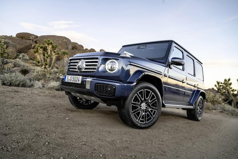 A dark blue Mercedes-Benz G-Class parked on a desert track among Joshua trees