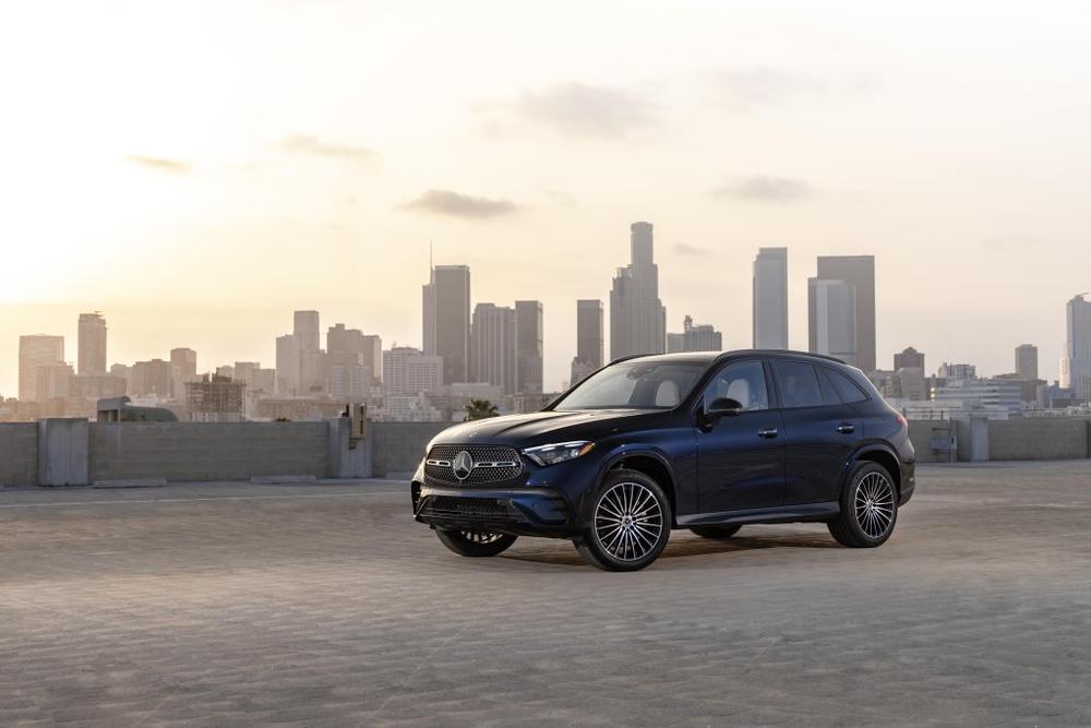 A dark blue Mercedes-Benz GLC parked on a rooftop with a city skyline behind it at sunset