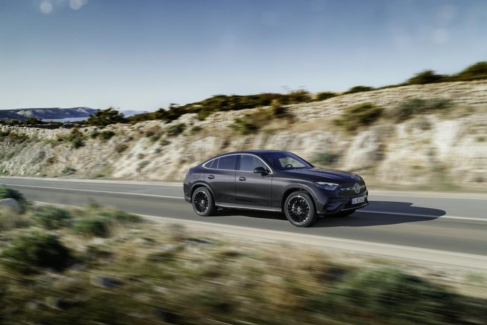 A dark grey Mercedes-Benz GLC Coupé driving along a coastal road with scrubby hills behind it