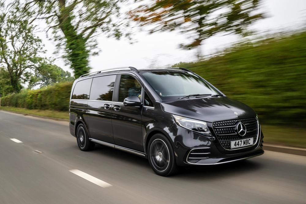 A black Mercedes-Benz V-Class driving along a country road past blurred hedges and trees